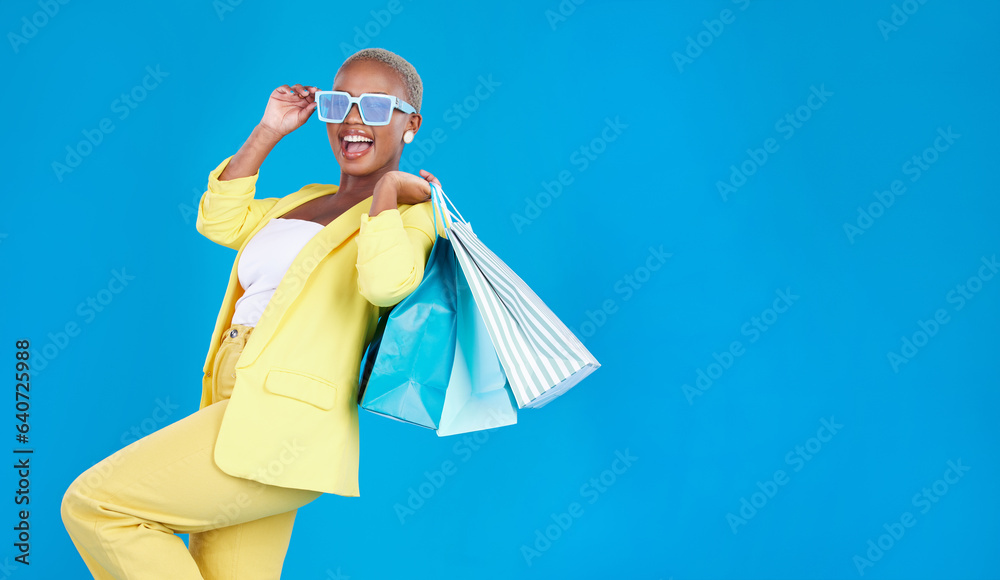 Fashion, sale and black woman with shopping, bag and glasses in studio excited and smile on blue bac