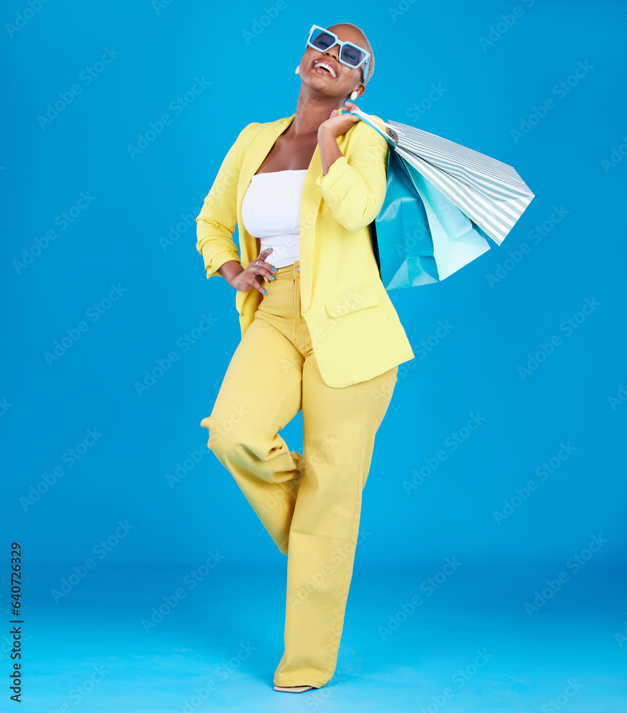 Fashion, smile and black woman in studio with shopping, bag and glasses or excited for sale on blue 