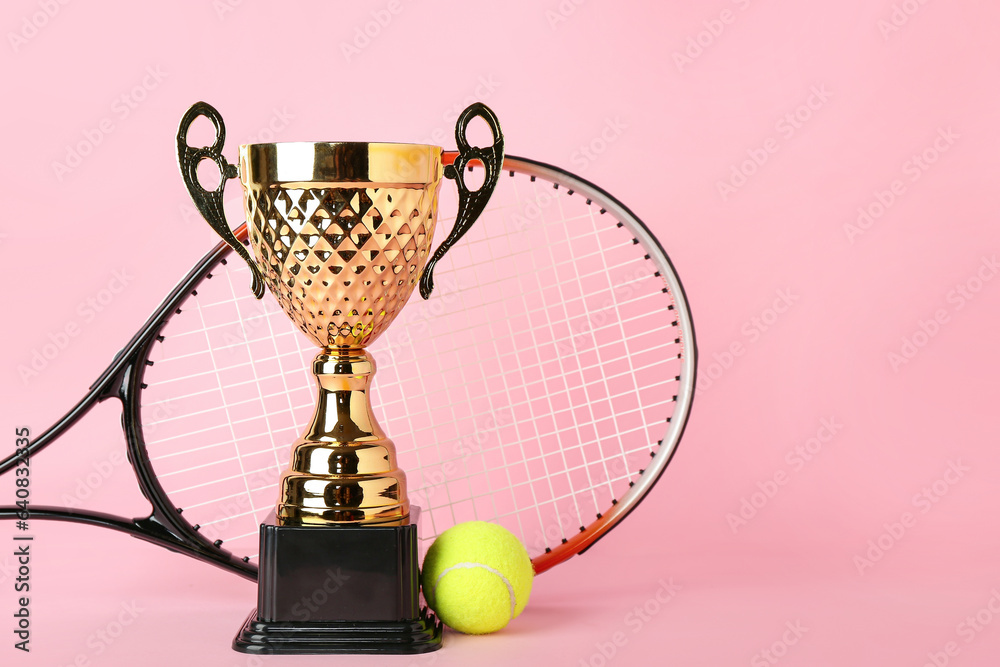 Gold cup with tennis racket and ball on pink background