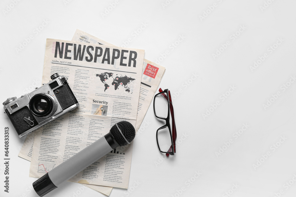 Newspaper with microphone, photo camera and eyeglasses on white background