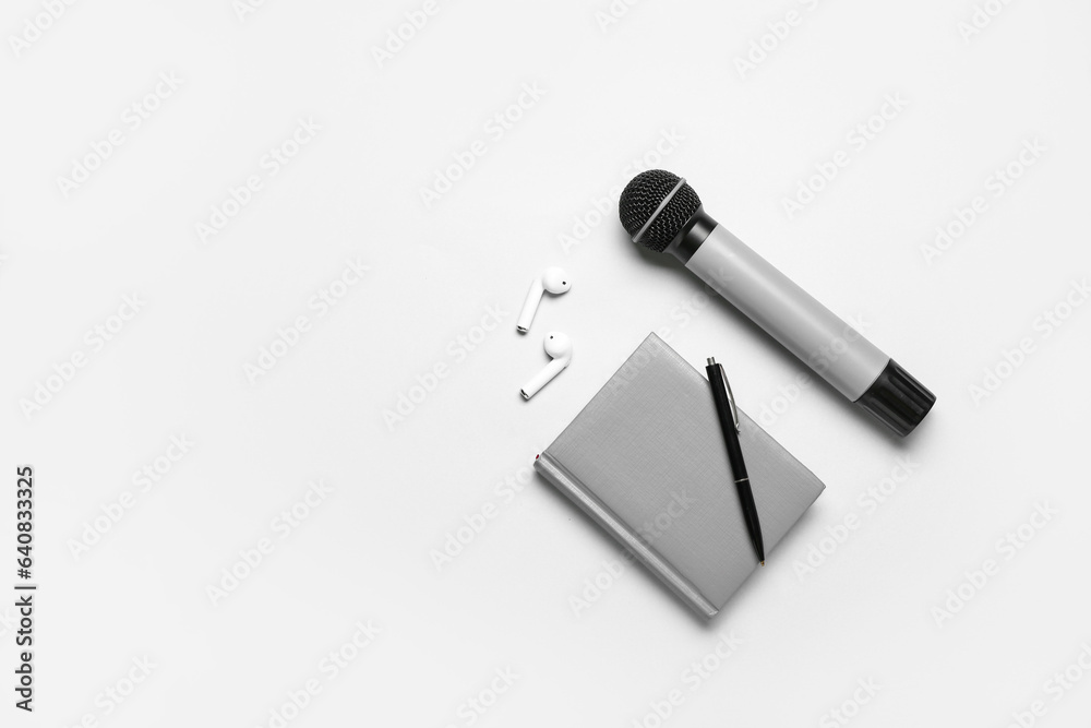 Notebook with pen, microphone and earphones on light background