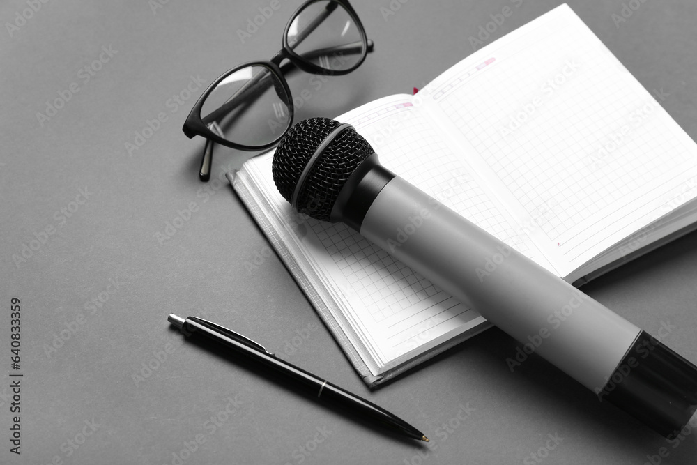 Notebook with pen, microphone and eyeglasses on dark background, closeup