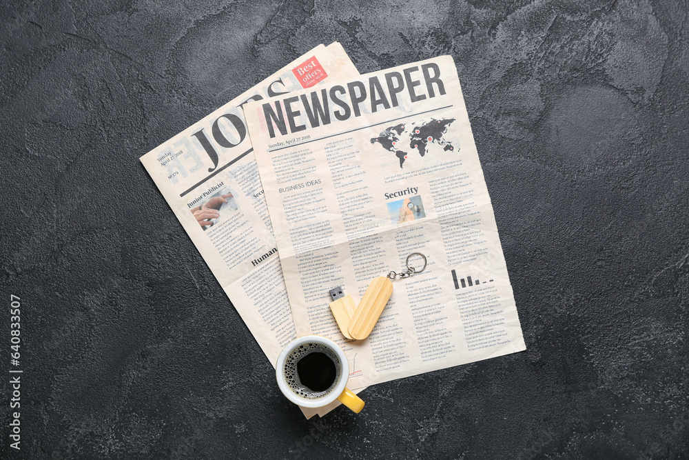 Newspapers with USB flash drive and cup of coffee on dark background