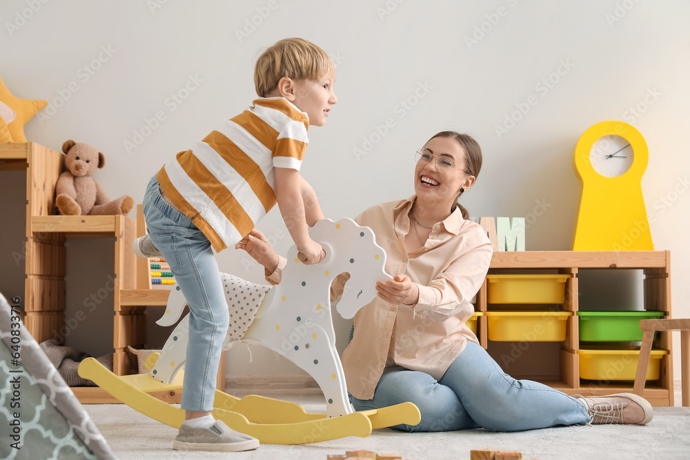 Nanny and little boy playing with rocking horse at home