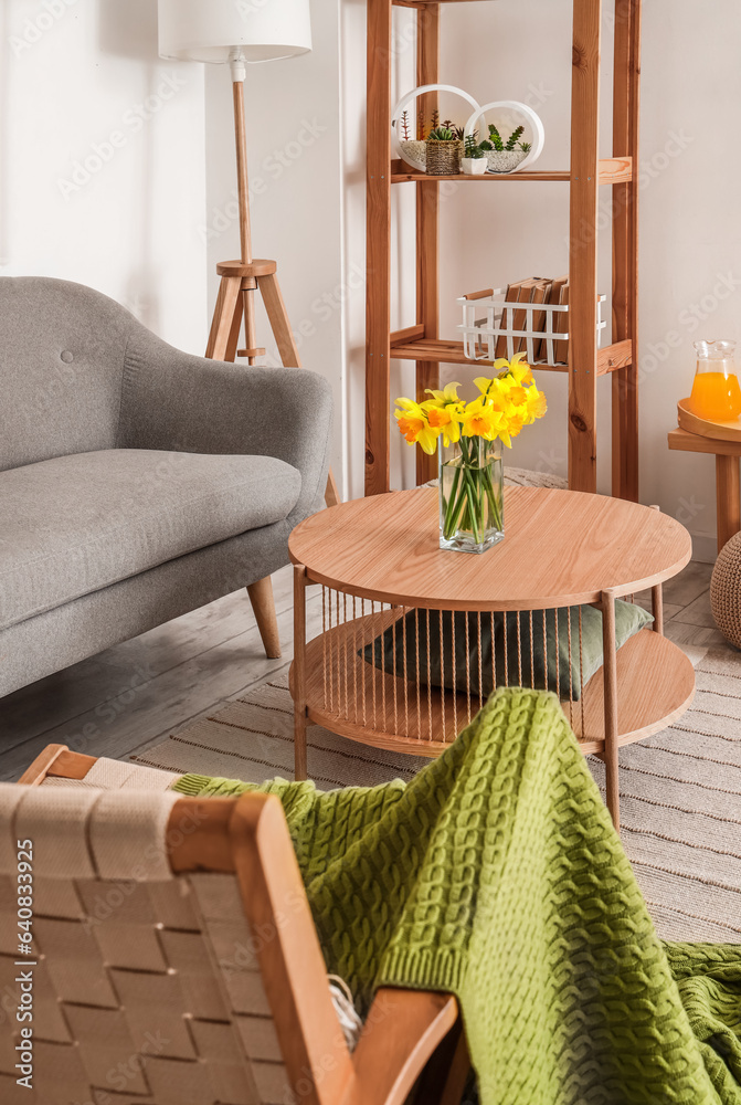 Interior of light living room with grey sofa, wooden armchair and coffee table