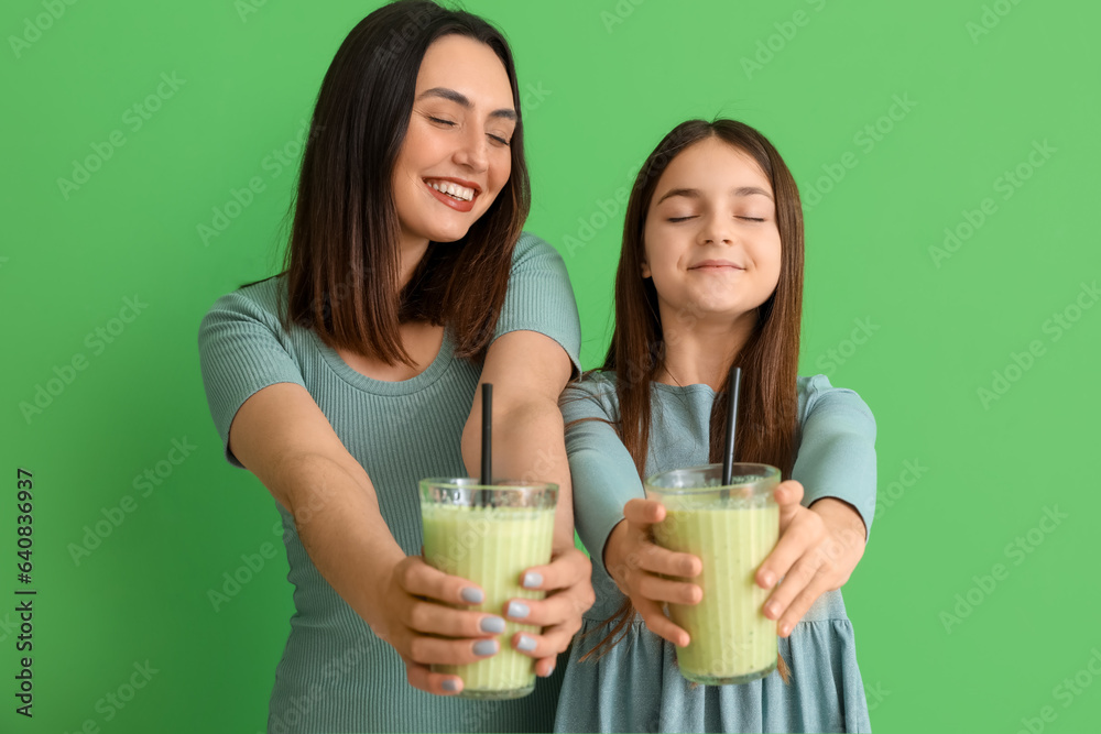 Little girl with her mother drinking smoothie on green background