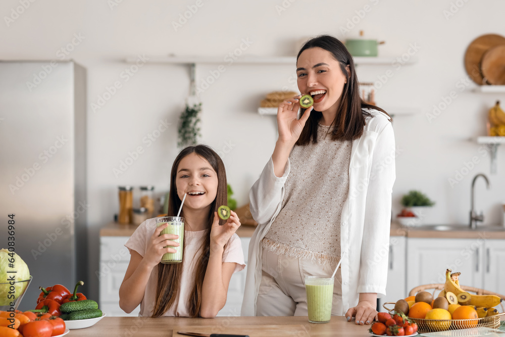 Little girl with her pregnant mother drinking green smoothie in kitchen