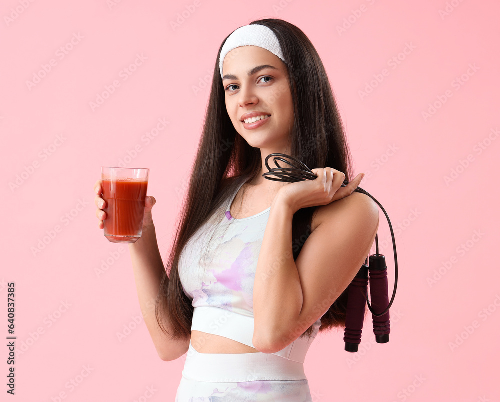 Sporty young woman with glass of vegetable juice and skipping rope on pink background