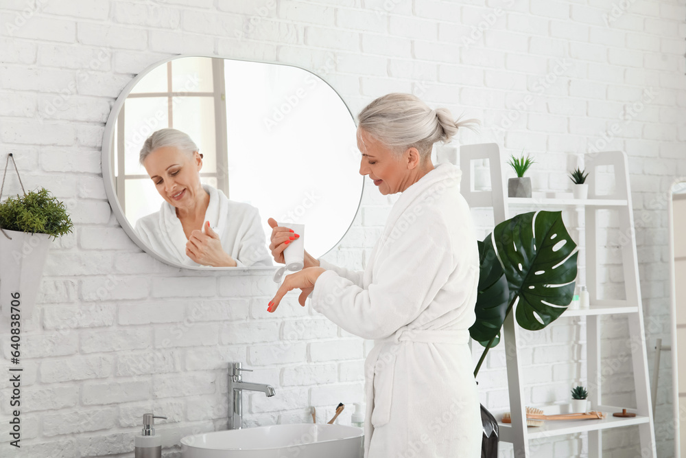 Mature woman applying hand cream in bathroom