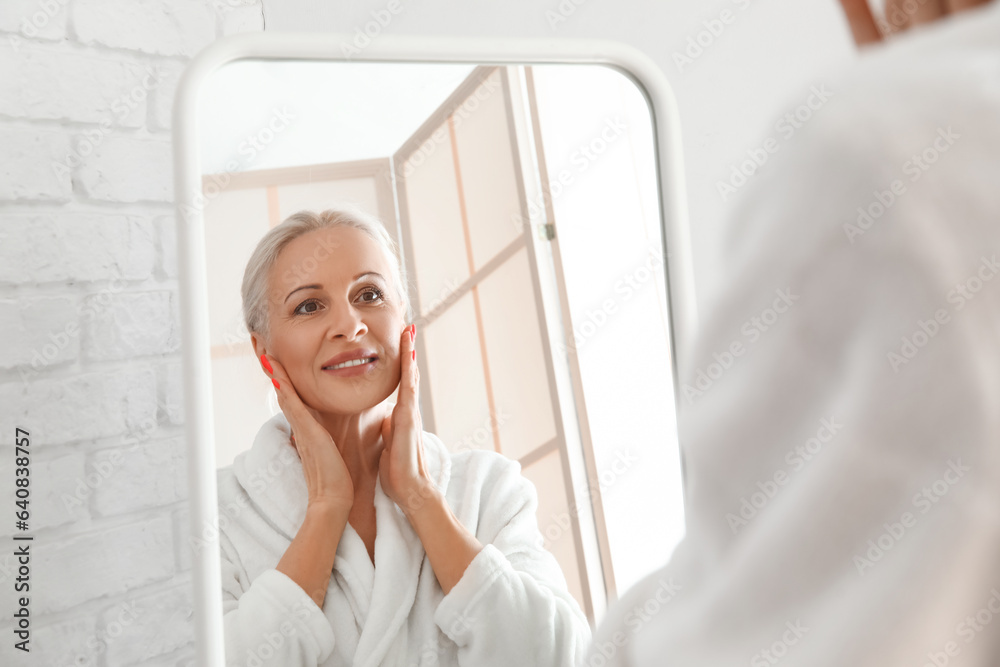 Mature woman applying oil near mirror in bathroom