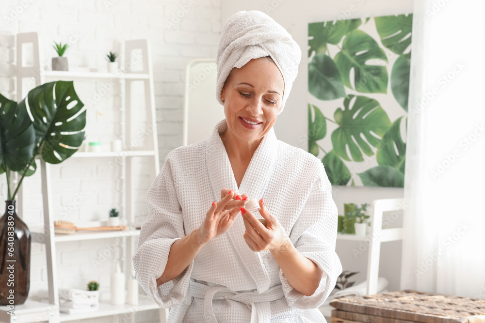 Mature woman with jar of facial cream in bathroom