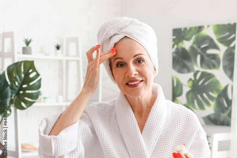 Mature woman applying facial cream in bathroom, closeup