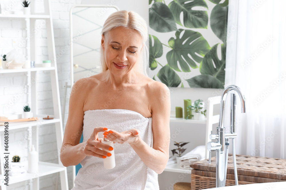 Mature woman applying facial cream in bathroom