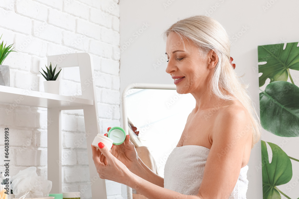 Mature woman with jar of cream in bathroom