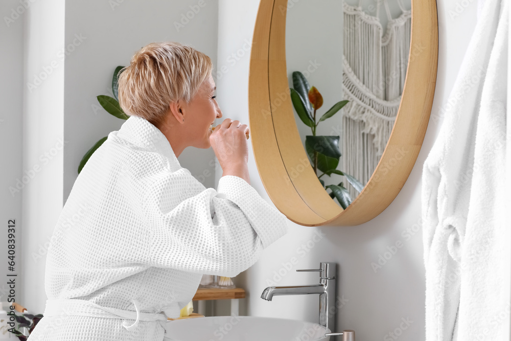 Mature woman brushing teeth near mirror in bathroom