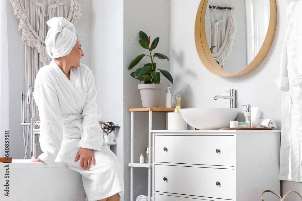 Mature woman with towel sitting in bathroom