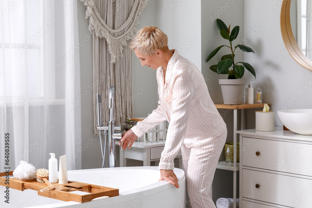 Mature woman turning on bathtub tap in bathroom