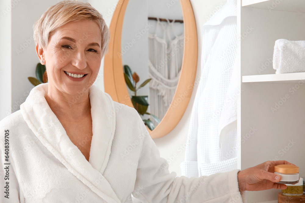 Mature woman taking jar of cream from shelf in bathroom, closeup