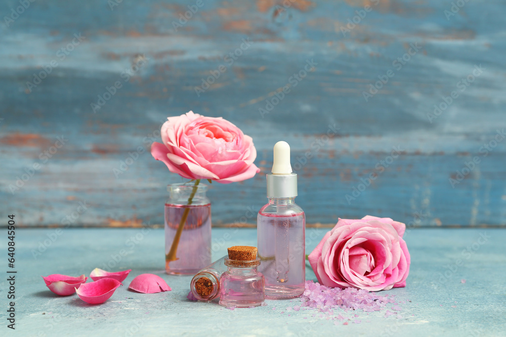 Bottles of cosmetic oil with rose extract and flowers on blue table