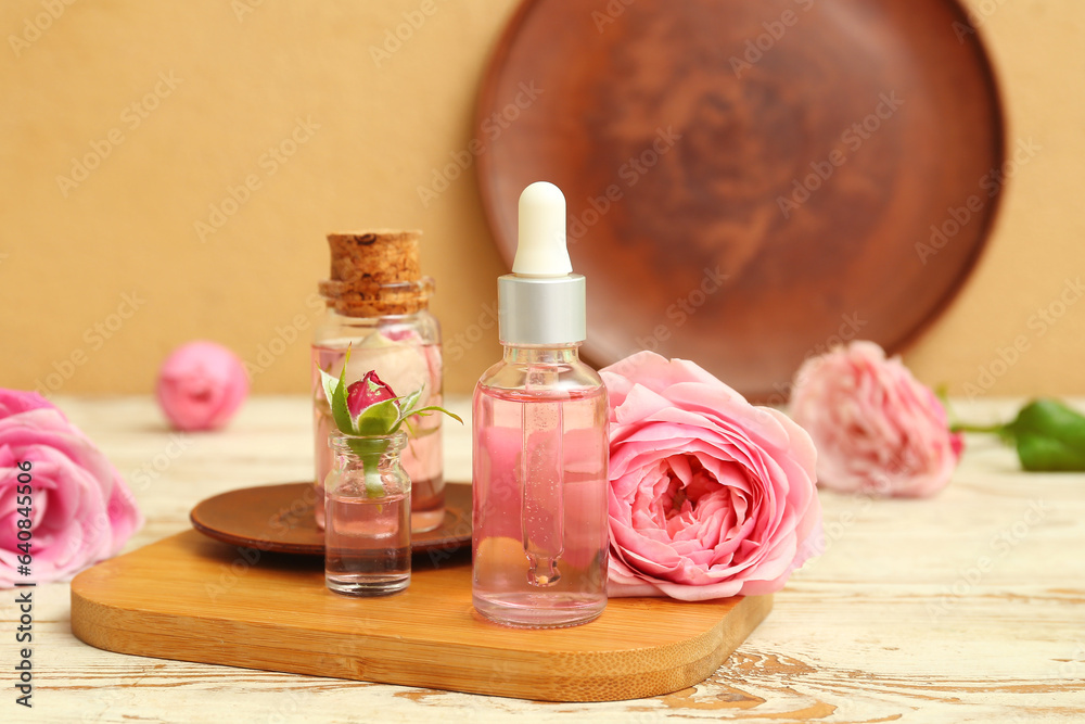 Bottles of cosmetic oil with rose extract and flowers on light wooden table