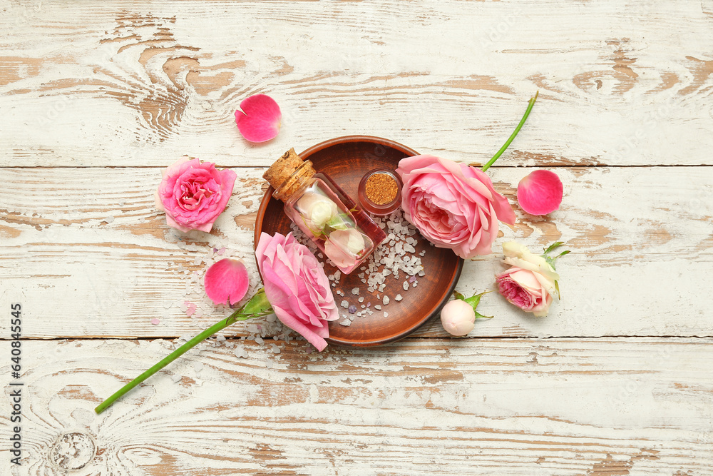 Bottles of cosmetic oil with rose extract and flowers on light wooden table