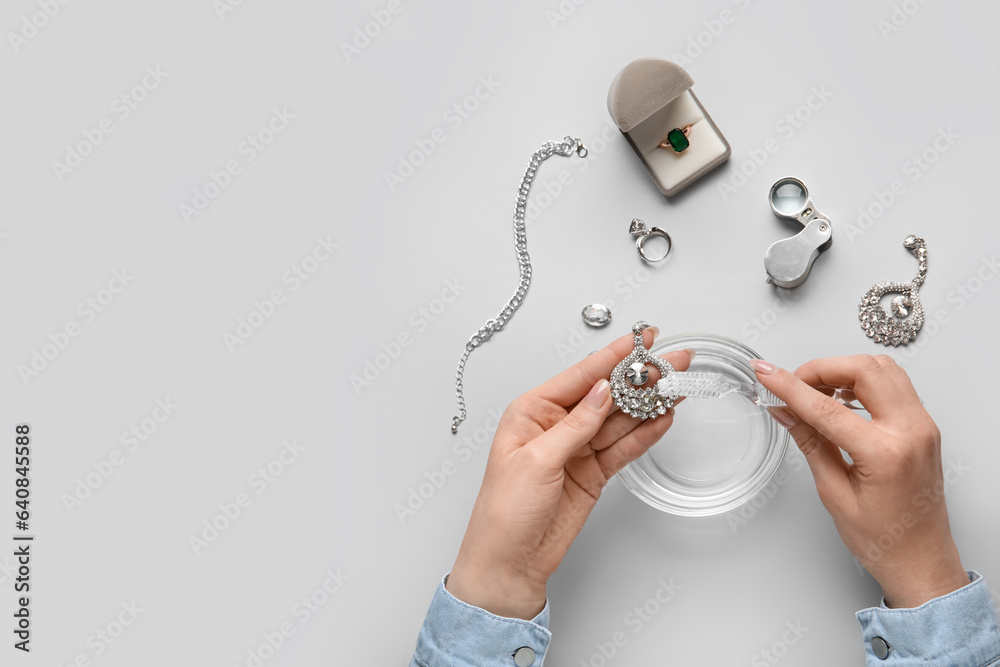 Woman cleaning beautiful jewelry with toothbrush on white background