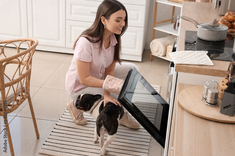 Young woman with her dog opening electric oven in kitchen