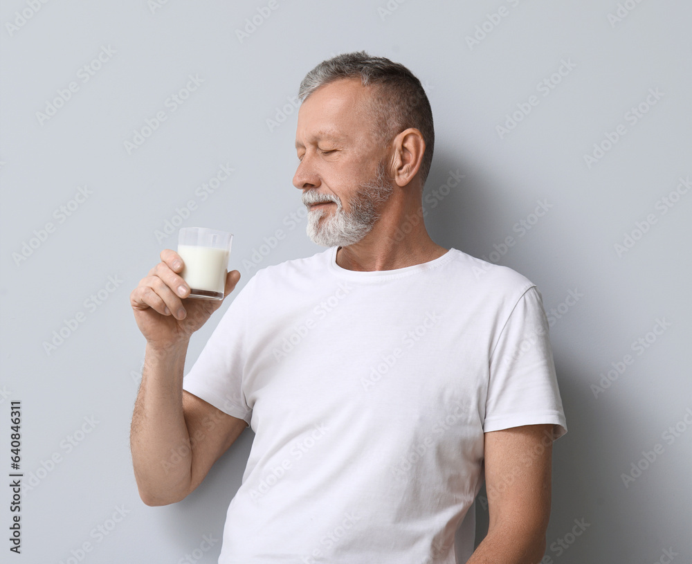 Mature man with glass of milk on light background