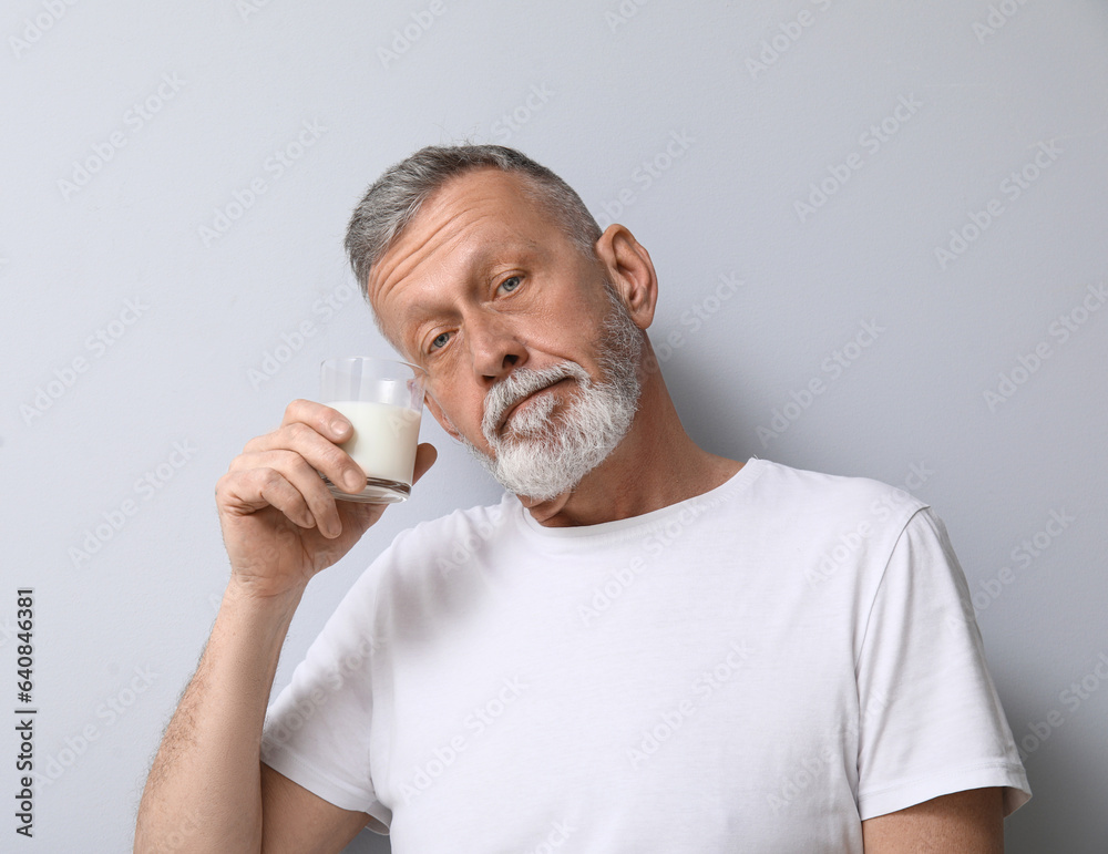 Mature man with glass of milk on light background