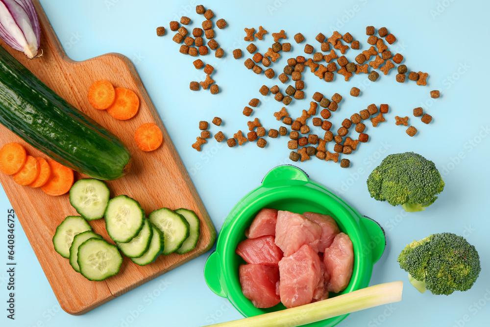 Composition with dry pet food, raw meat and natural products on blue background