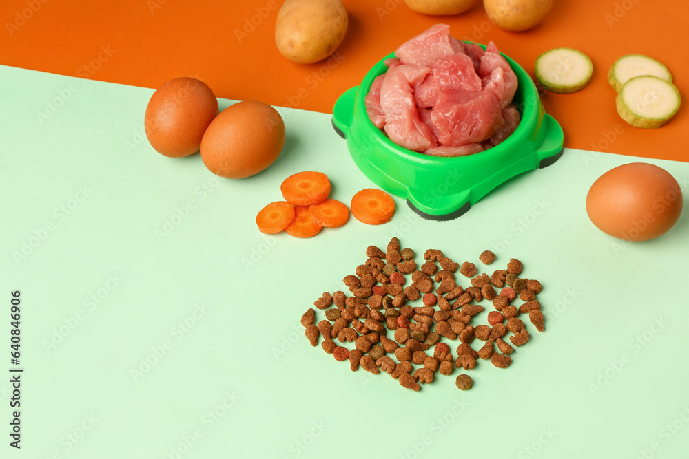 Bowl with raw meat, dry pet food and natural products on color background