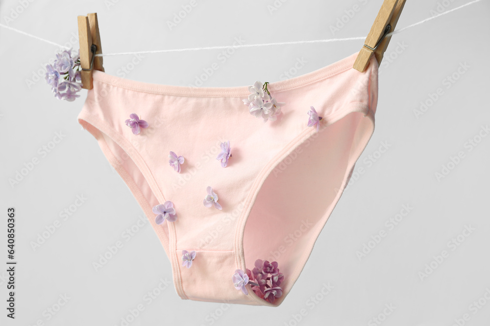 Stylish female panties with beautiful lilac flowers hanging on rope against white background, closeu