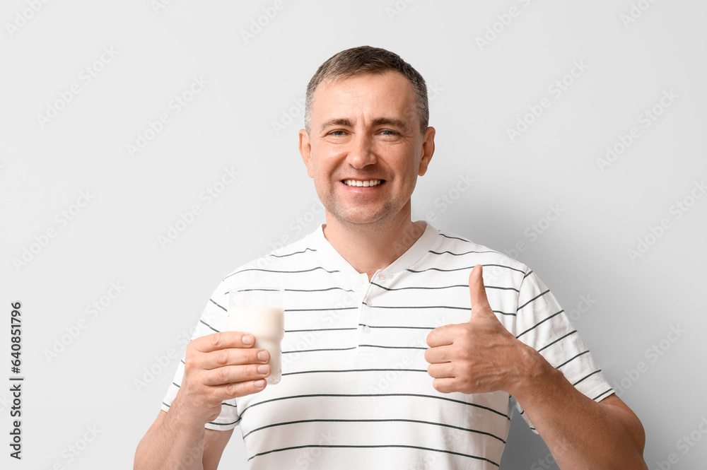 Mature man with glass of milk showing thumb-up on white background