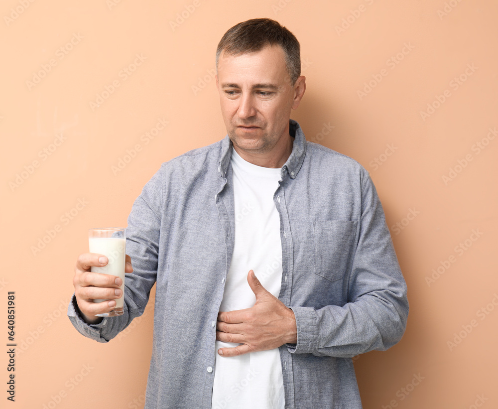 Displeased mature man with glass of milk on beige background