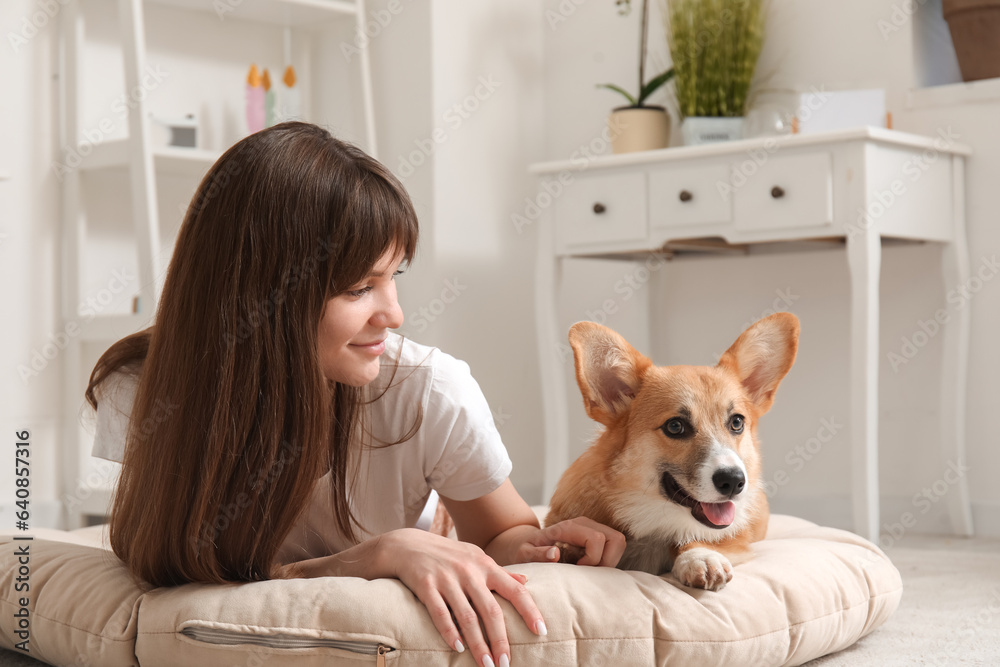 Pretty young woman lying on pet bed with cute Corgi dog in living room