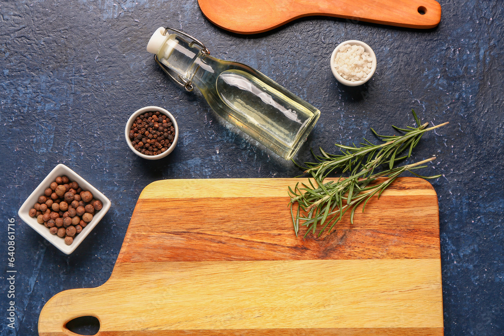 Wooden cutting board, bottle of oil and spices on dark color background