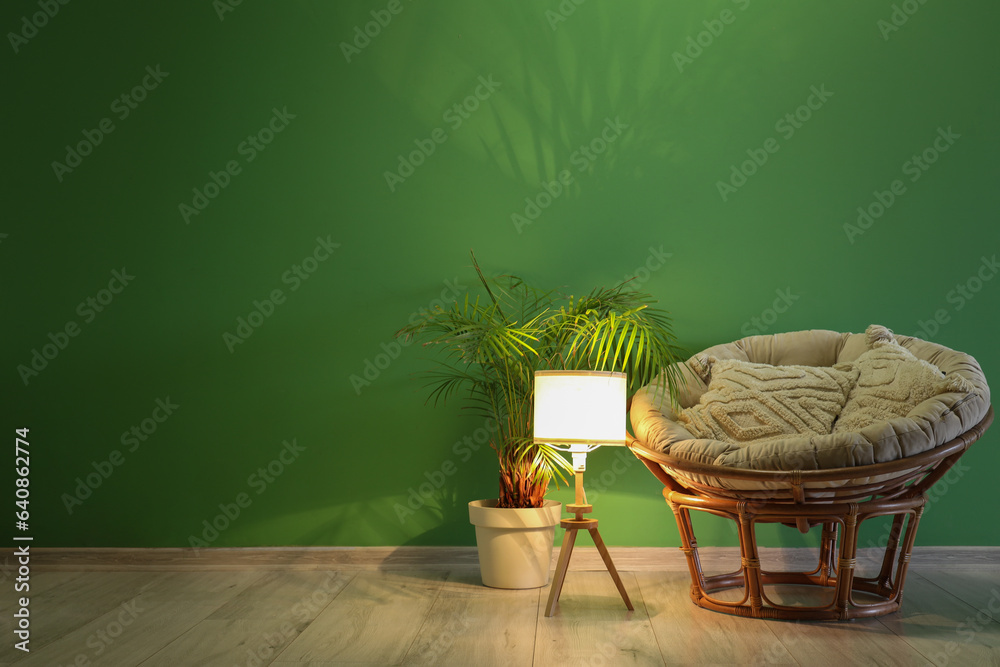 Glowing lamp with armchair and palm tree near green wall in room