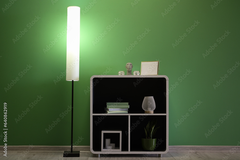 Glowing lamp and shelving unit with decor near green wall in room