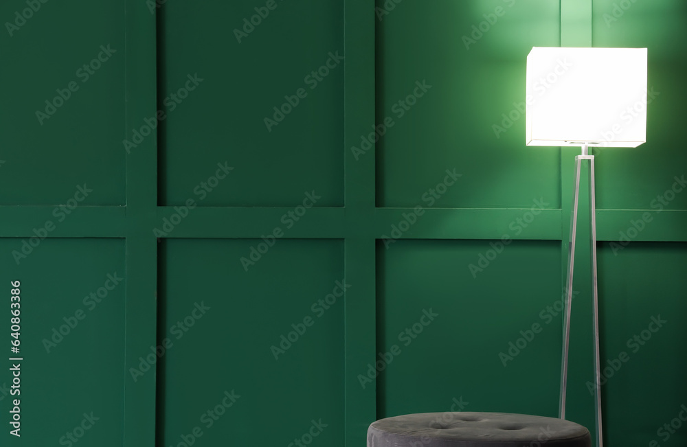 Glowing stand lamp with pouf near green wall in room