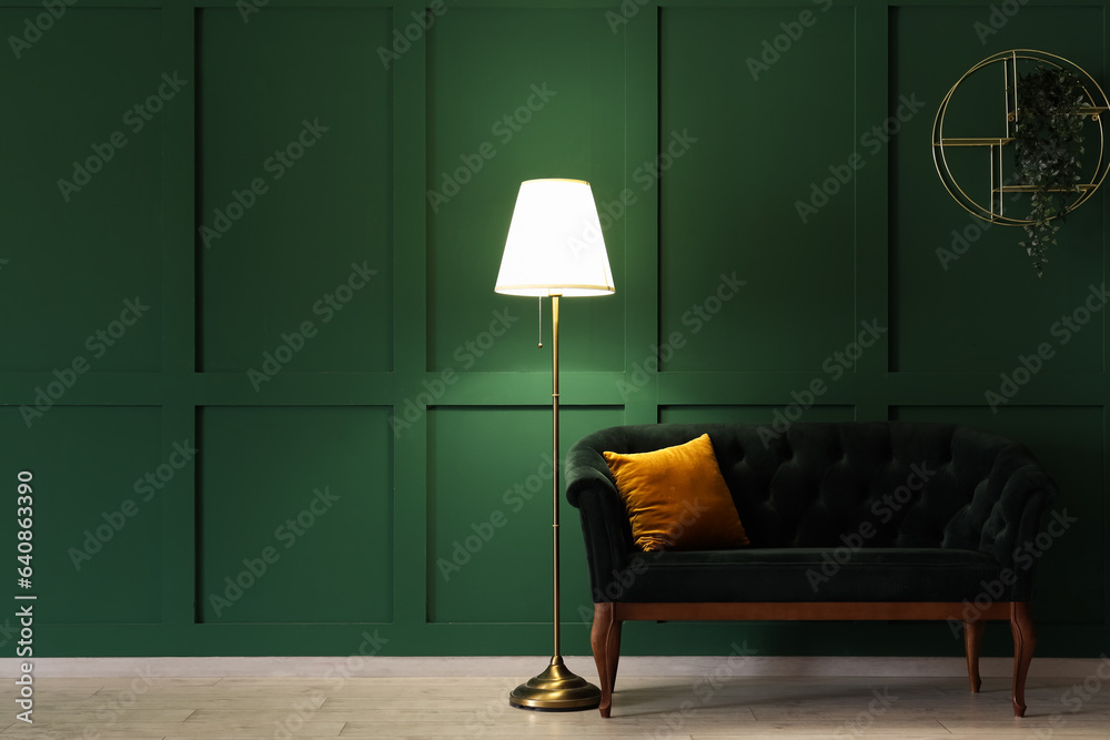 Glowing stand lamp with sofa near green wall in dark room