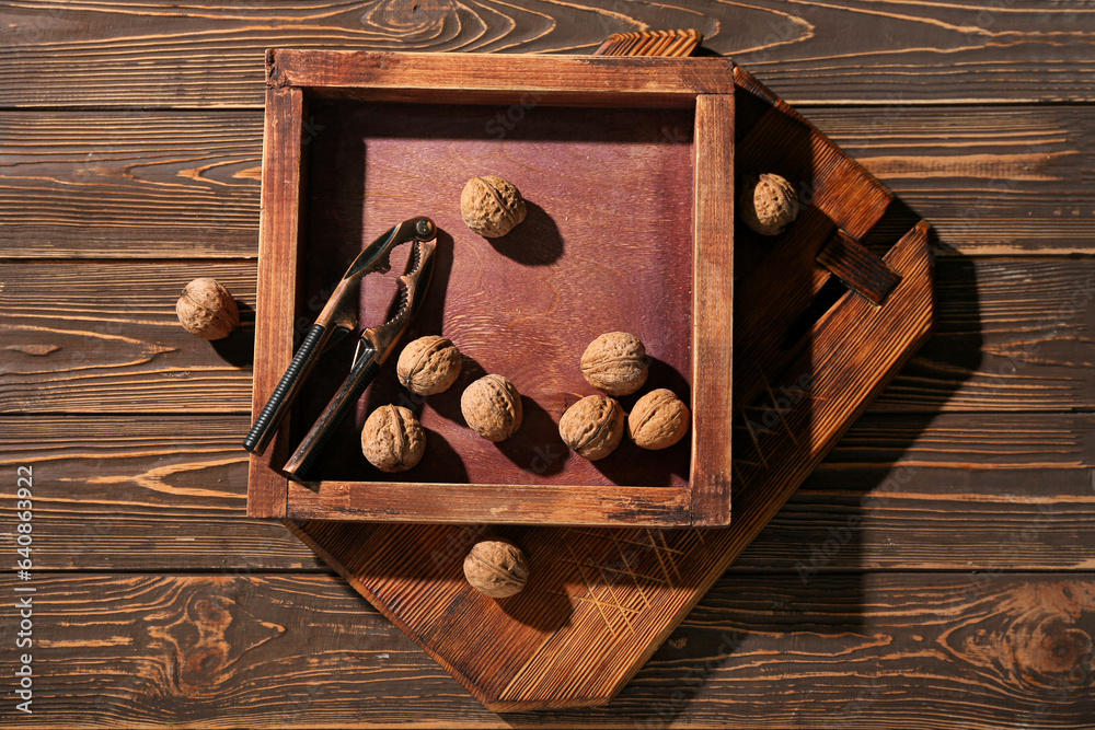 Different cutting boards with walnuts and nutcracker on wooden background