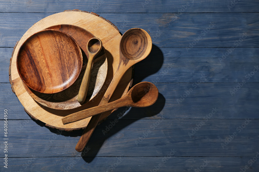 New cutting board, plates and spoons on blue wooden background