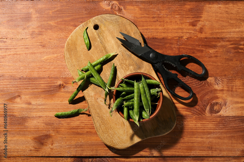 New cutting board, scissors and bowl with green peas on wooden background