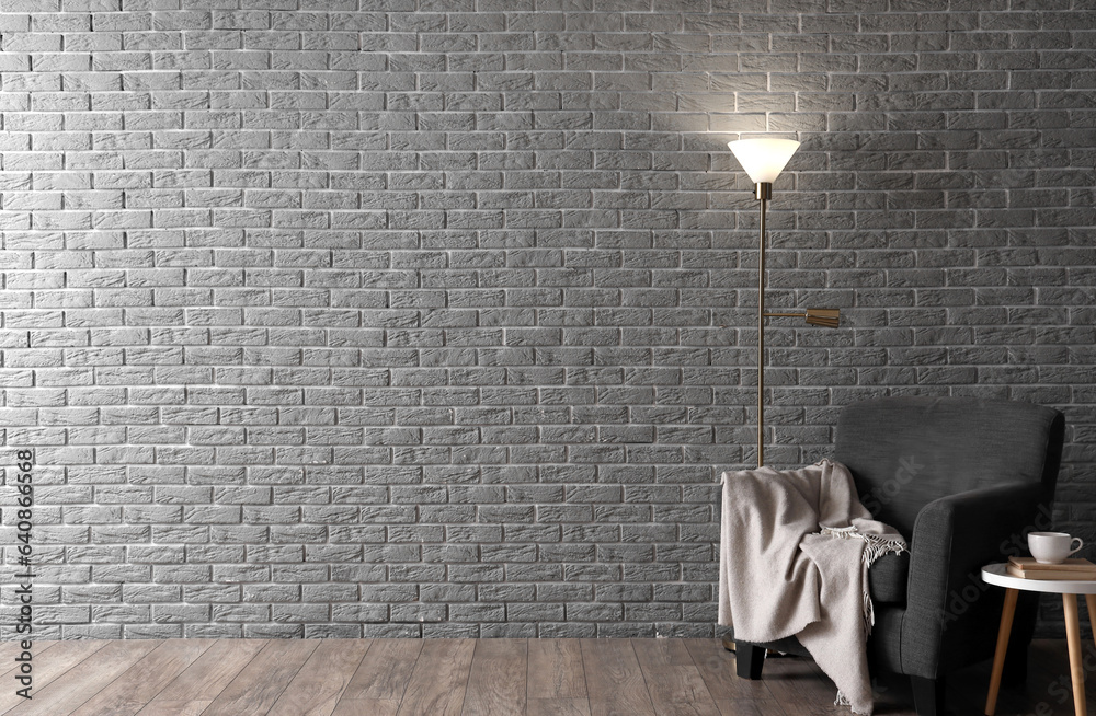 Glowing lamp and cozy armchair near grey brick wall