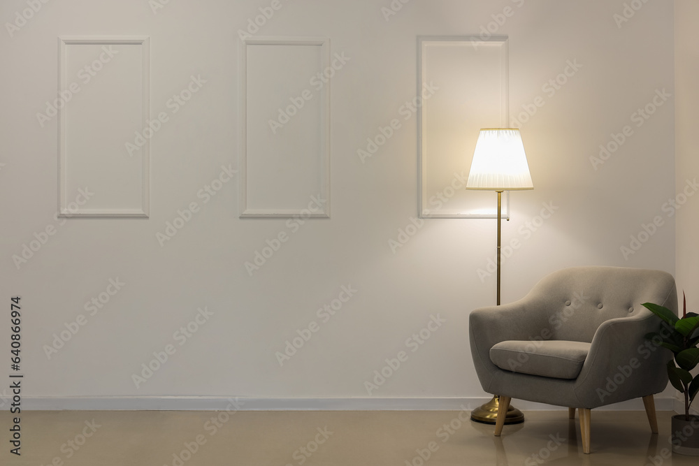 Glowing lamp and grey armchair near white wall