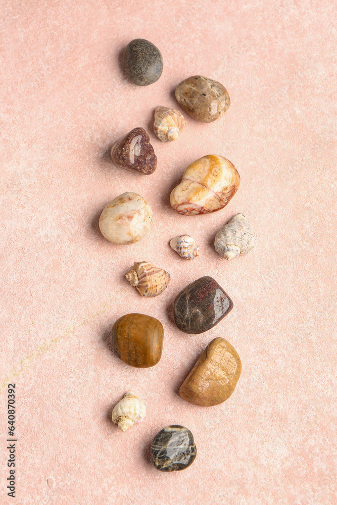 Many pebble stones and seashells on pink background