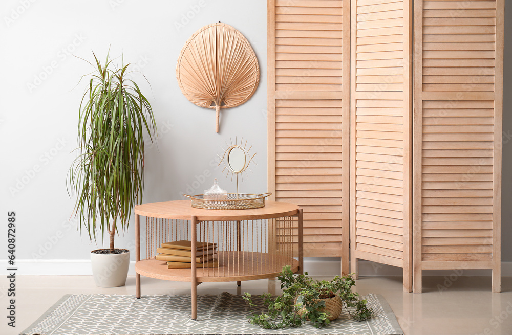 Interior of living room with wooden coffee table, houseplants and folding screen