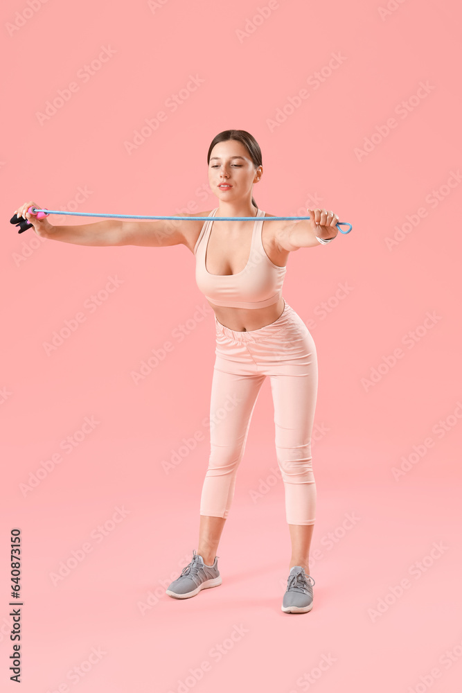 Sporty young woman training with skipping rope on pink background