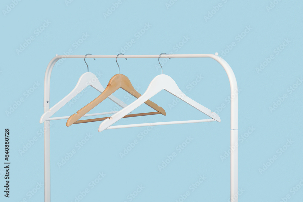 Rack with wooden clothes hangers on blue background