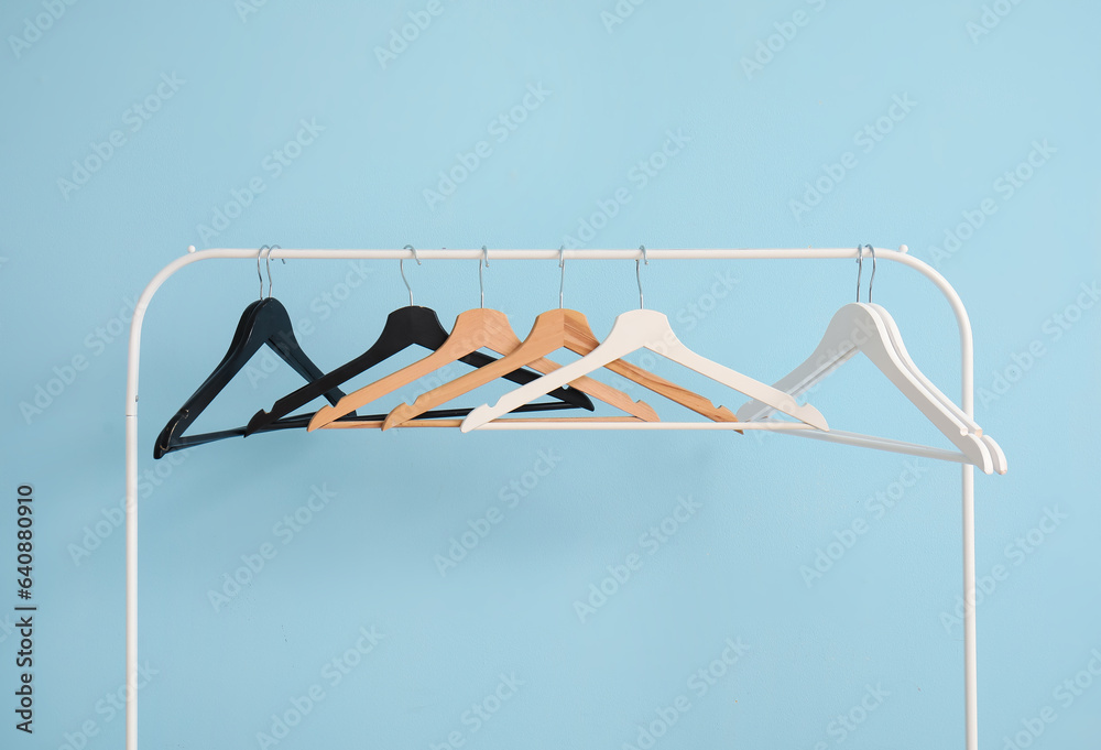 Rack with wooden clothes hangers on blue background